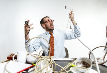 Completely confused. There are a lot of wires in the workplace and man is constantly tangled in them. It's literally blocking him. Concept of office worker's troubles, business, problems and stress.